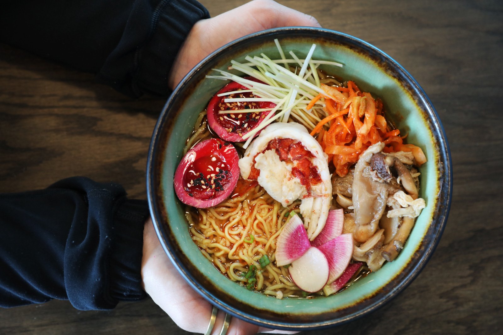 holding a bowl full of ramen